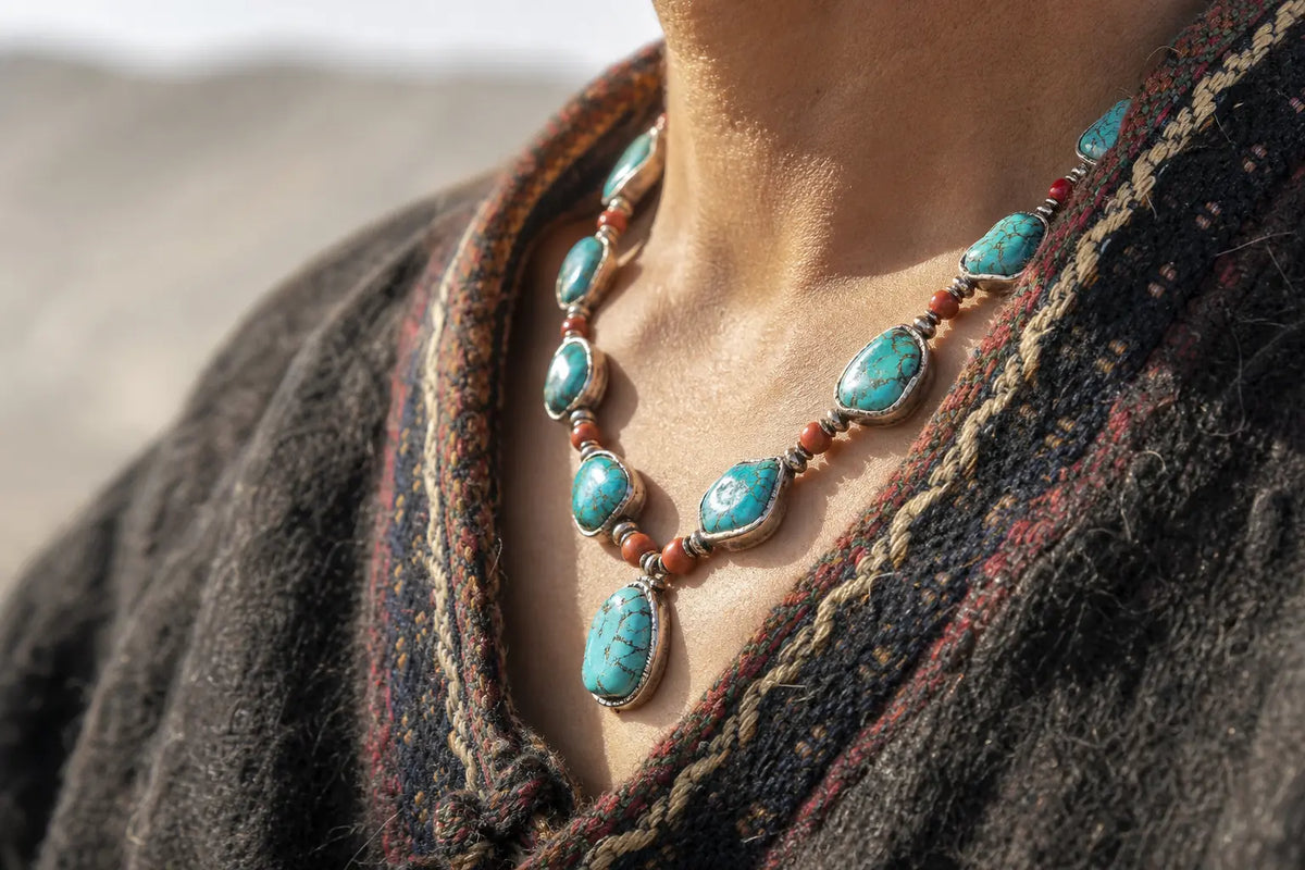 Rough sky-blue turquoise cabochons and red coral beads set in hand-worked silver, worn at the throat over a dark wool collar, cropped with no face in frame